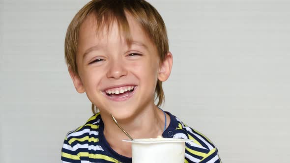 The Little Boy Laughs at the Camera. The Child Sits at the Table and Eats Yogurt. Happy Emotions