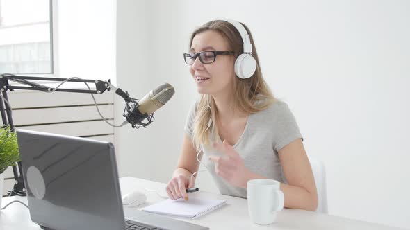 Concept of Streaming and Broadcasting. Young Cheerful Girl in the Studio Speaks Into a Microphone