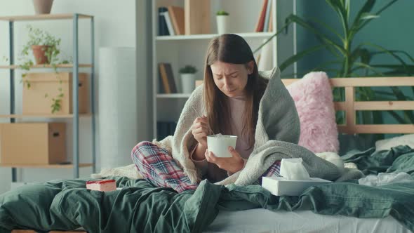 A Stressed Young Woman Wrapped In a Blanket Sits on a Sofa Eats Ice Cream