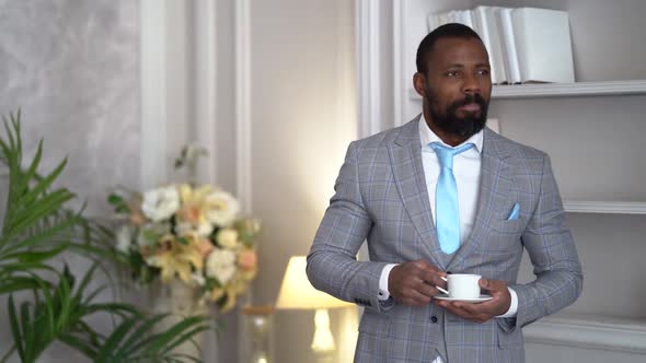 Handsome Rich Man Is Standing in Hall of Luxury Apartment and Holding Cup of Coffee or Tea