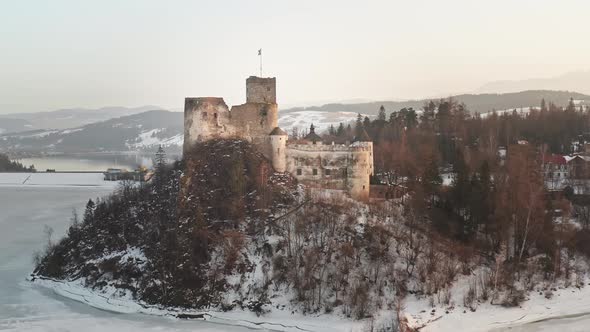 Idyllic Niedzica Castle at dusk on top of hill at frozen lake Czorsztyn, aerial