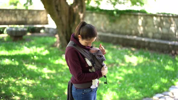 Mom Strokes Newborn Baby in Sling in the Park