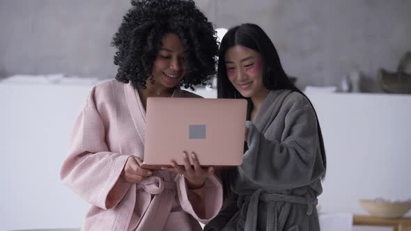 Positive African American and Asian Roommates Surfing Social Media on Laptop in Slow Motion Smiling
