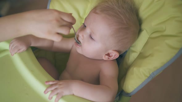 Mommy Feeds Funny Boy with Tasty Meal in Soft Highchair