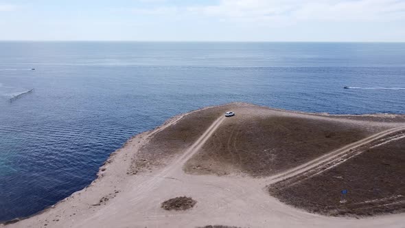 Aircraft Tracks a Car That Is Traveling on the Steppe Along the Sea Against the Blue Sky