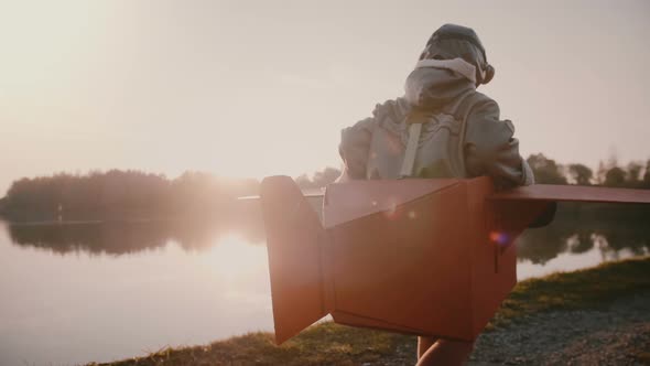 Camera Follows Little Happy European Boy Pretending To Be a Plane Pilot in Fun Costume at Sunset