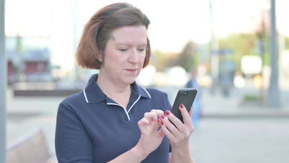 Old Woman Celebrating Online Success on Smartphone Outdoor