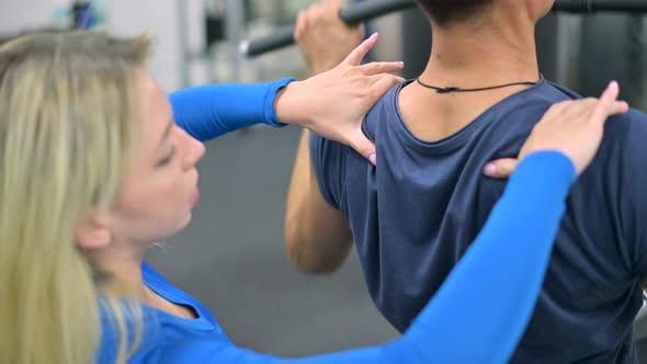 Close-up of trainer woman hands on man shoulders on exercise machine