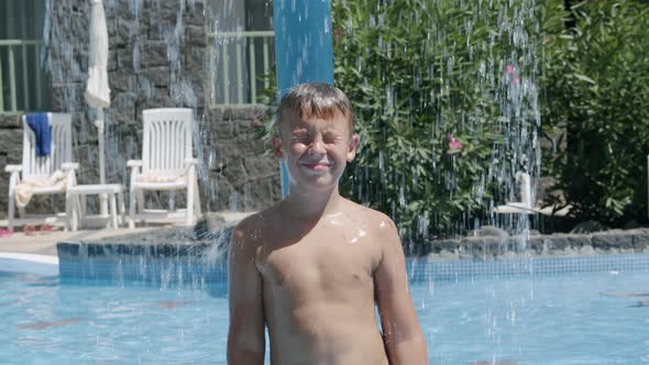 Boy refreshing under waterfall in outside swimming pool