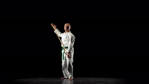 Kendo Fighter on White Kimono Practicing Martial Art with the Bamboo Bokken on Black Background.