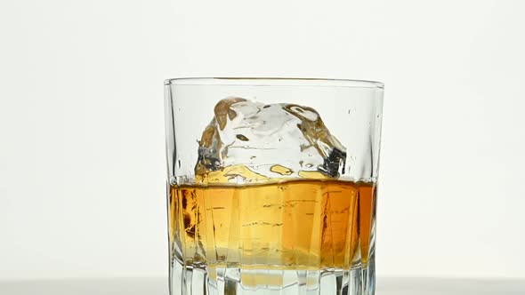 One big ice rock spins in whiskey glass on white