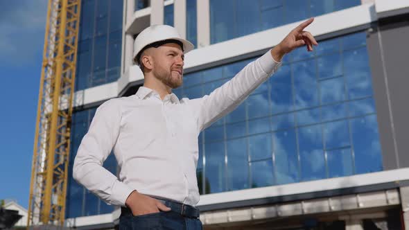 Engineer Architect in a White Shirt and Helmet on the Background of a Modern Glass Building Manages