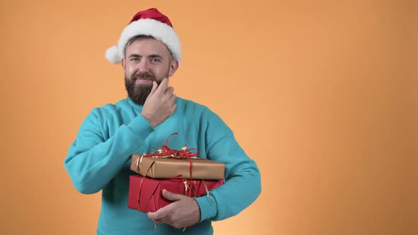 A guy in a santa claus hat with gifts in his hands