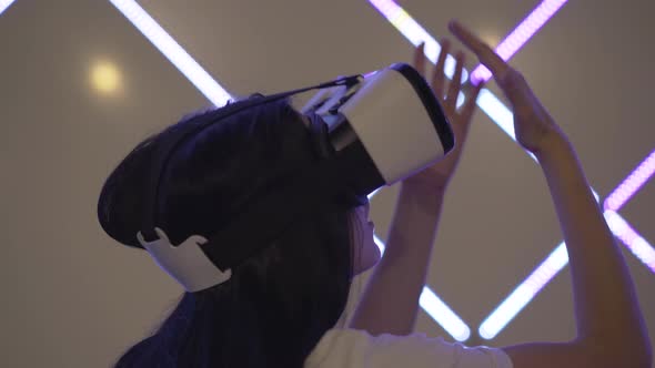 Back Side View of Cheerful Excited Woman in VR-glasses Standing in Neon Lights and Moving Hands