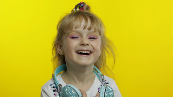 Child Smiling, Looking at Camera. Girl with Headphones on the Neck Posing on Yellow Background