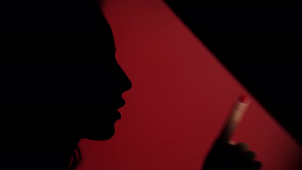 Side View of Faded Female Face Placing Her Finger on Lips on Dark Red Background