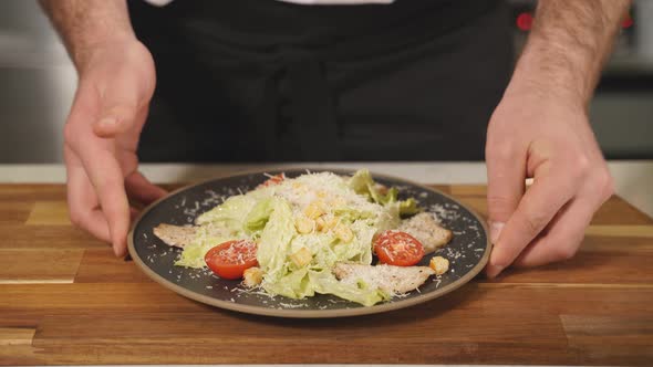 The Chef Serves Caesar Salad on a Black Plate on a Wooden Table