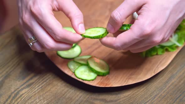 Women's Hands Spread the Sliced Cucumber on a Wooden Cutting Board Next to Pita
