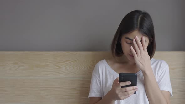 Upset young woman sitting on bed, holding smartphone in hands, received message with bad news.