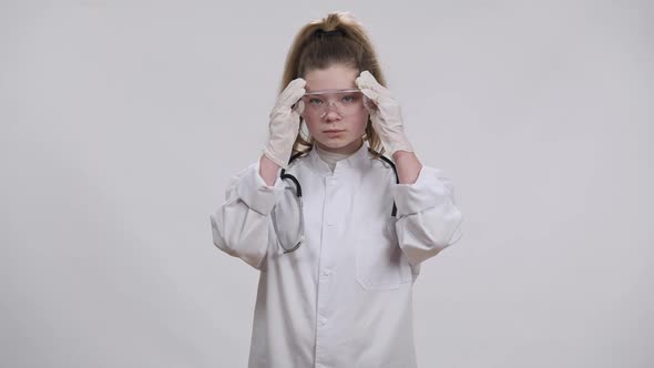 Front View Portrait of Charming Confident Little Doctor Putting on Transparent Eyeglasses Looking at