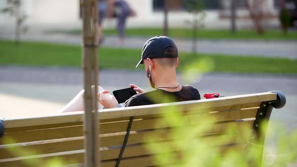 The Young Man Sits in the Park and Chats on the Smartphone. Happy Man Use Smartphone Sitting on