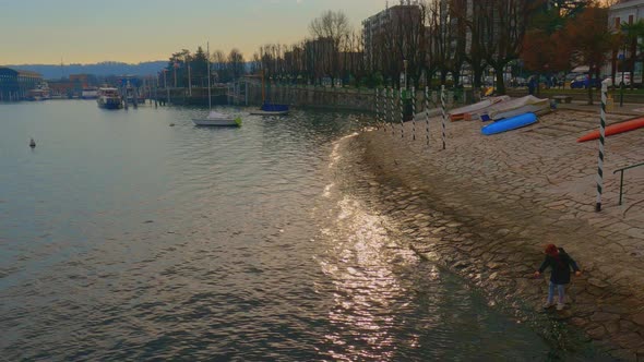 Little girl with red hair plays on lake shore, Arona on Maggiore Lake. High angle