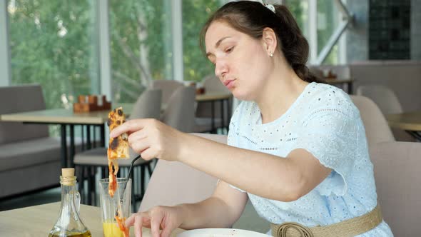 Pretty Brunette Woman in Blue Dress Eats Pizza in Restaurant