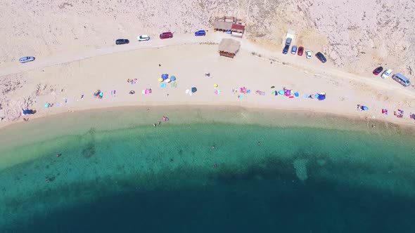 Flying above umbrellas and people on isolated beach of Pag island, Croatia