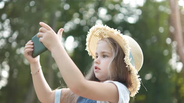 Happy smiling child girl looking in mobile phone outdoors in summer.