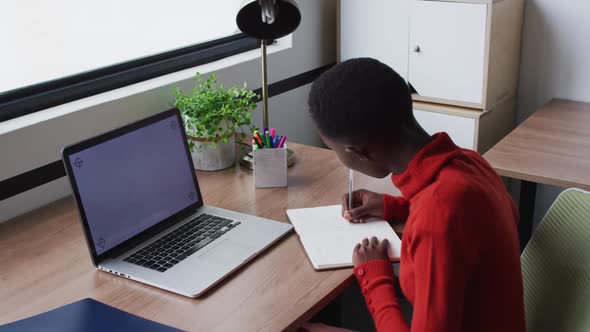 African american businesswoman writing and smiling, on video call using laptop, copy space on screen