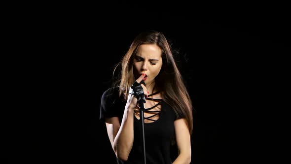 Singer Sexually Dances and Sings Songs in a Microphone at a Concert. Black Background