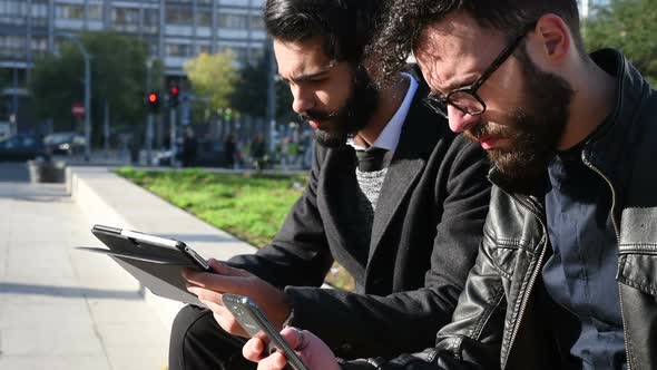 Two young businessmen outdoor using smartphone and tablet