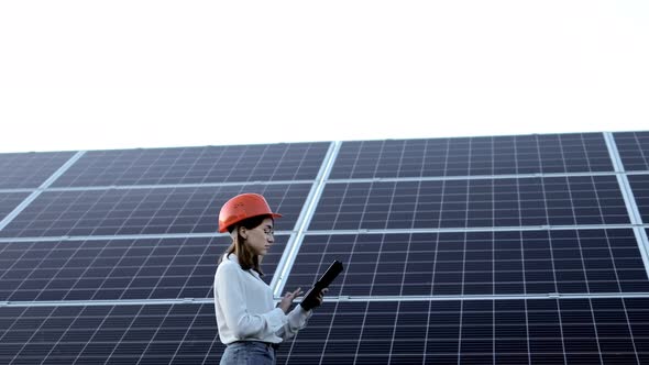 Beautiful young engineer standing near solar panels outdoors, Green Energy Concept