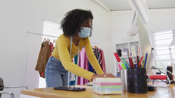 Female fashion designer wearing face mask using computer at studio