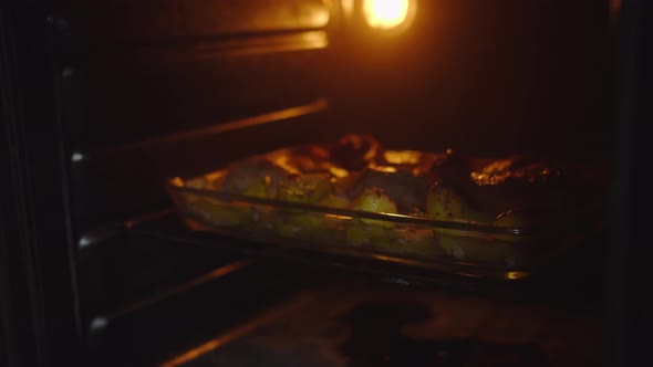 Man Takes Out a Baking Sheet with Baked Food Chicken Legs and Potatoes