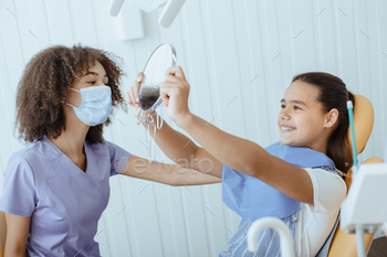 irl looks in mirror for estimating dentist work and enjoying result with young african american specialist in uniform, protective mask and gloves