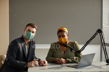 the table in protective mask and looking at camera during interview on radio