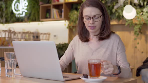 Working Woman Browsing Laptop and Drinking Tea at Table