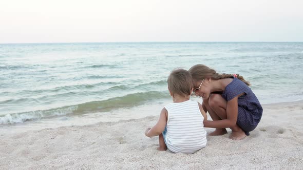 Girl Helping Her Little Brother to Look for Seashells in the Sand on the Coast