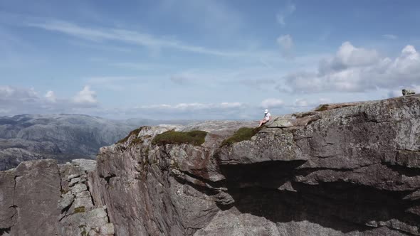 Aerial Shot of a Cliff with a Woman Sitting Revealing the Landscape of Norway