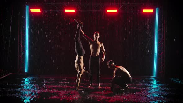 Men Perform Acrobatic Stunts in the Rain. Professional Performance of Three Male Acrobats. Black