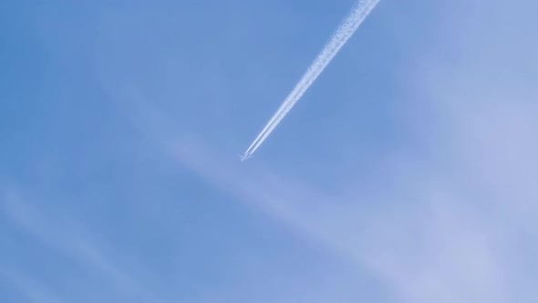 Distant Passenger Jet Plane Flying on High Altitude on Blue Sky with White Clouds Leaving Smoke