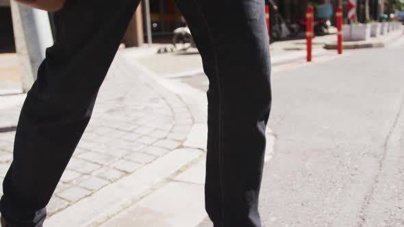 Midsection of african american businessman holding coffee walking in city street