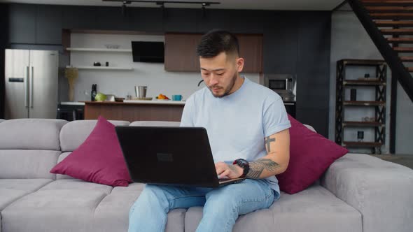 Asian Hipster Man Networking Online on Laptop on Couch