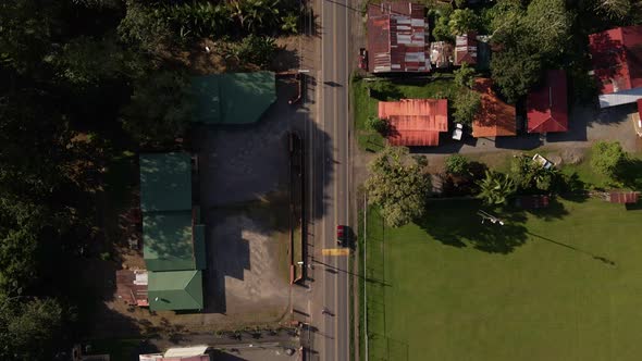 Aerial high angle tracking shot following a red pick up truck along a straight road through a town.