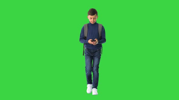 Schoolboy with a Backpack Using Mobile Phone While Walking on a Green Screen, Chroma Key.