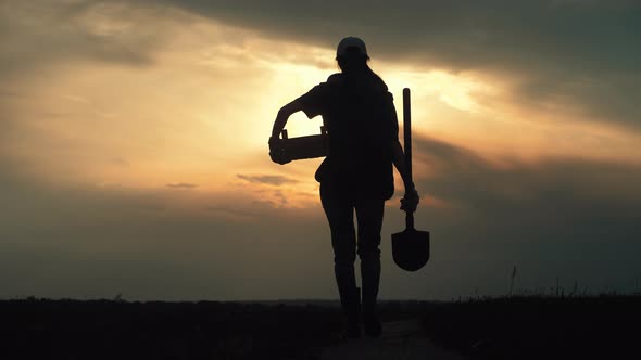 Young Gardener Woman Wearing Gumboots and Harvesting Tools in Hand Goes Along a Village Road at