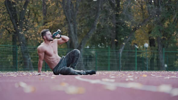 Shirtless sportsman drinks water on the stadium