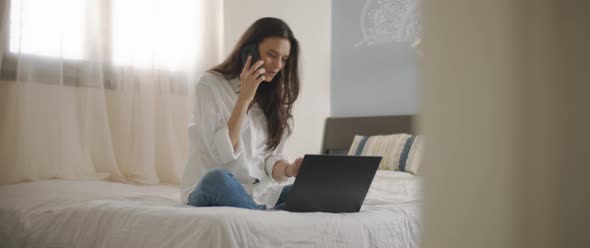 A woman talking to someone on the phone while working with a laptop from home