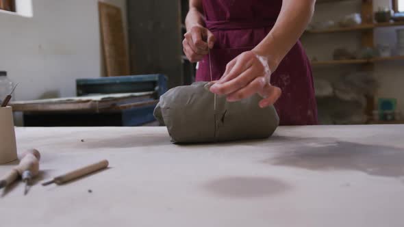 Mid section of female potter cutting clay with thread at pottery studio